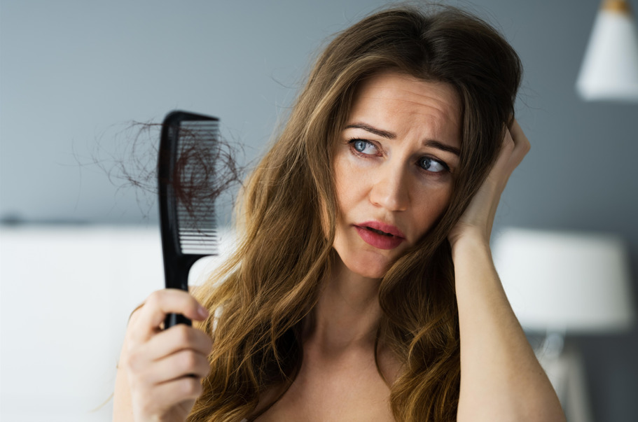 Mulher com queda de cabelo segurando pente, fazendo referência ao Eflúvio Telógeno.