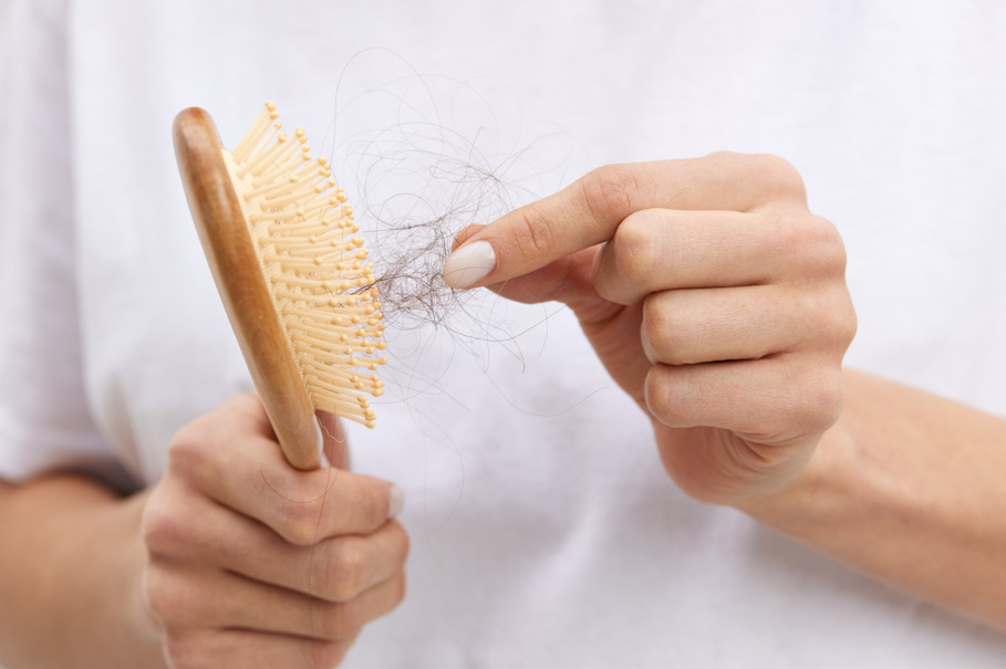 Imagem de duas mãos, uma segurando a escova de cabelo com e a outra os fios de cabelo.