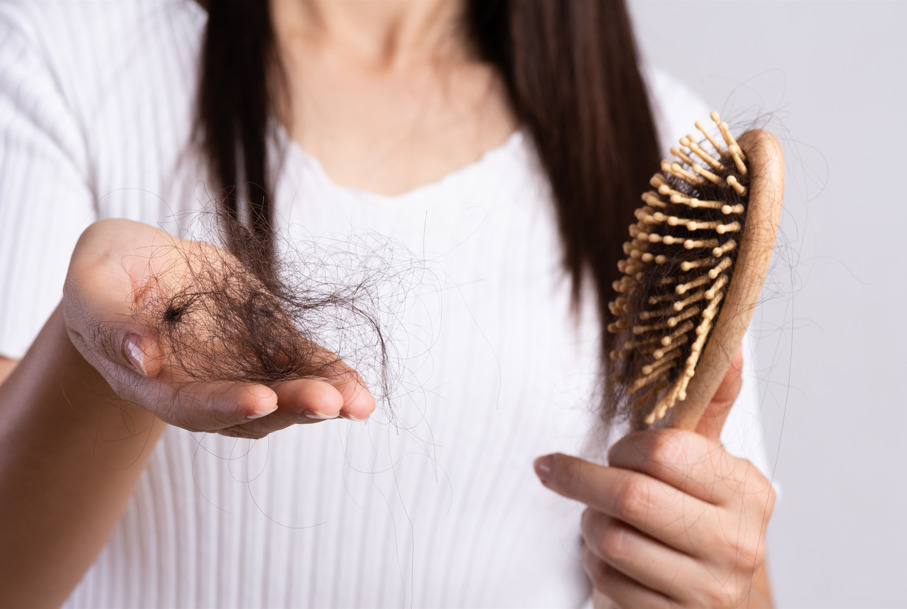 Mulher com escova e fios de cabelo nas mãos, fazendo referência à queda de cabelo após Covid-19.