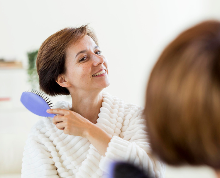 Tricologia no Brasil: mulher sorrindo e escovando o cabelo.